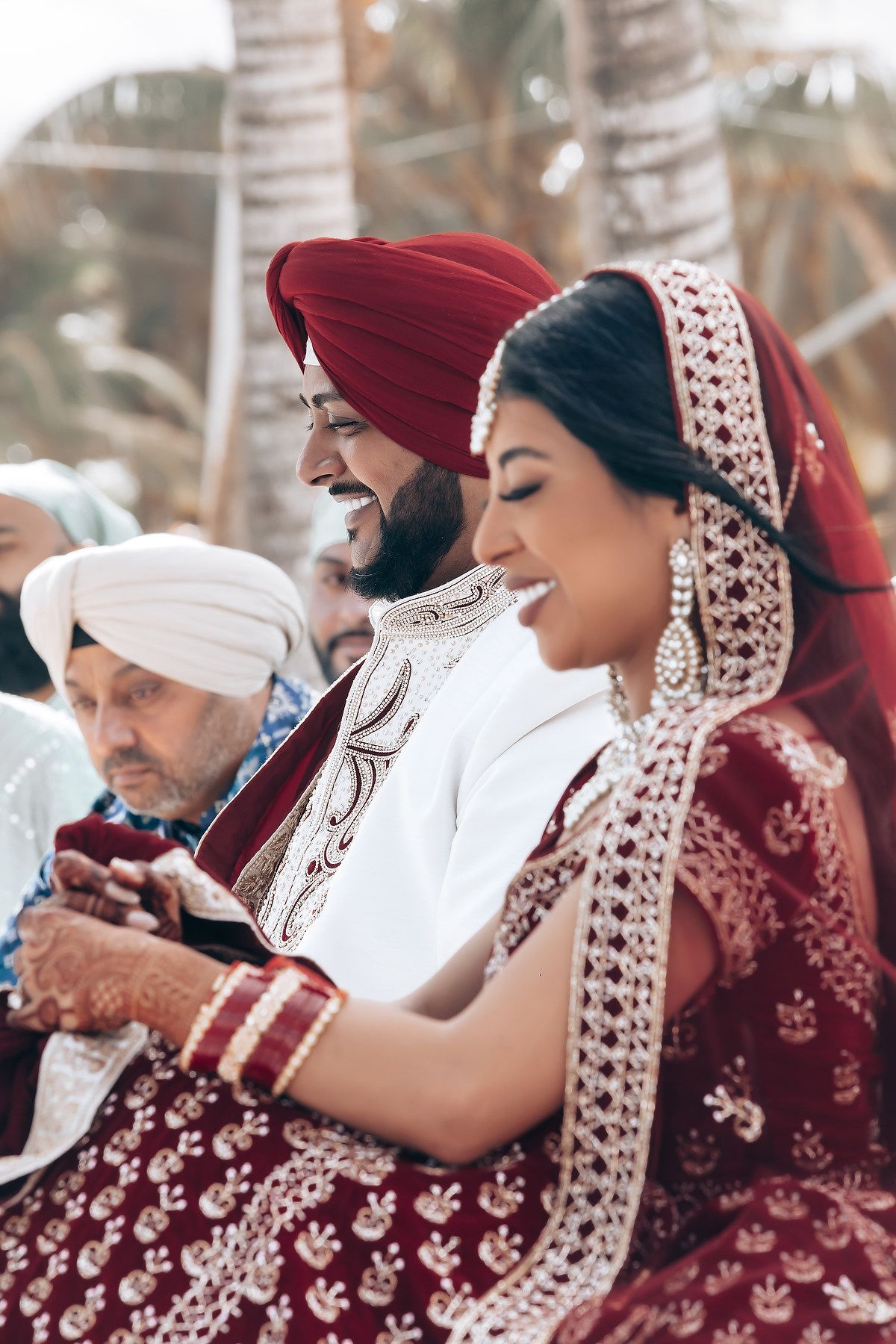 Traditional Sikh wedding ceremony participants in burgundy and white attire during prayers.