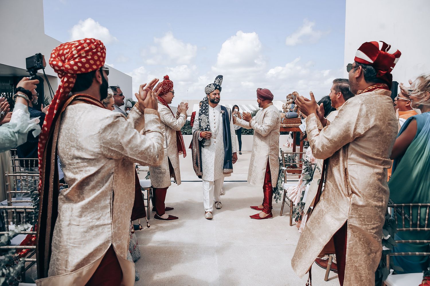 Wedding guests in formal attire gather under a bright blue sky.