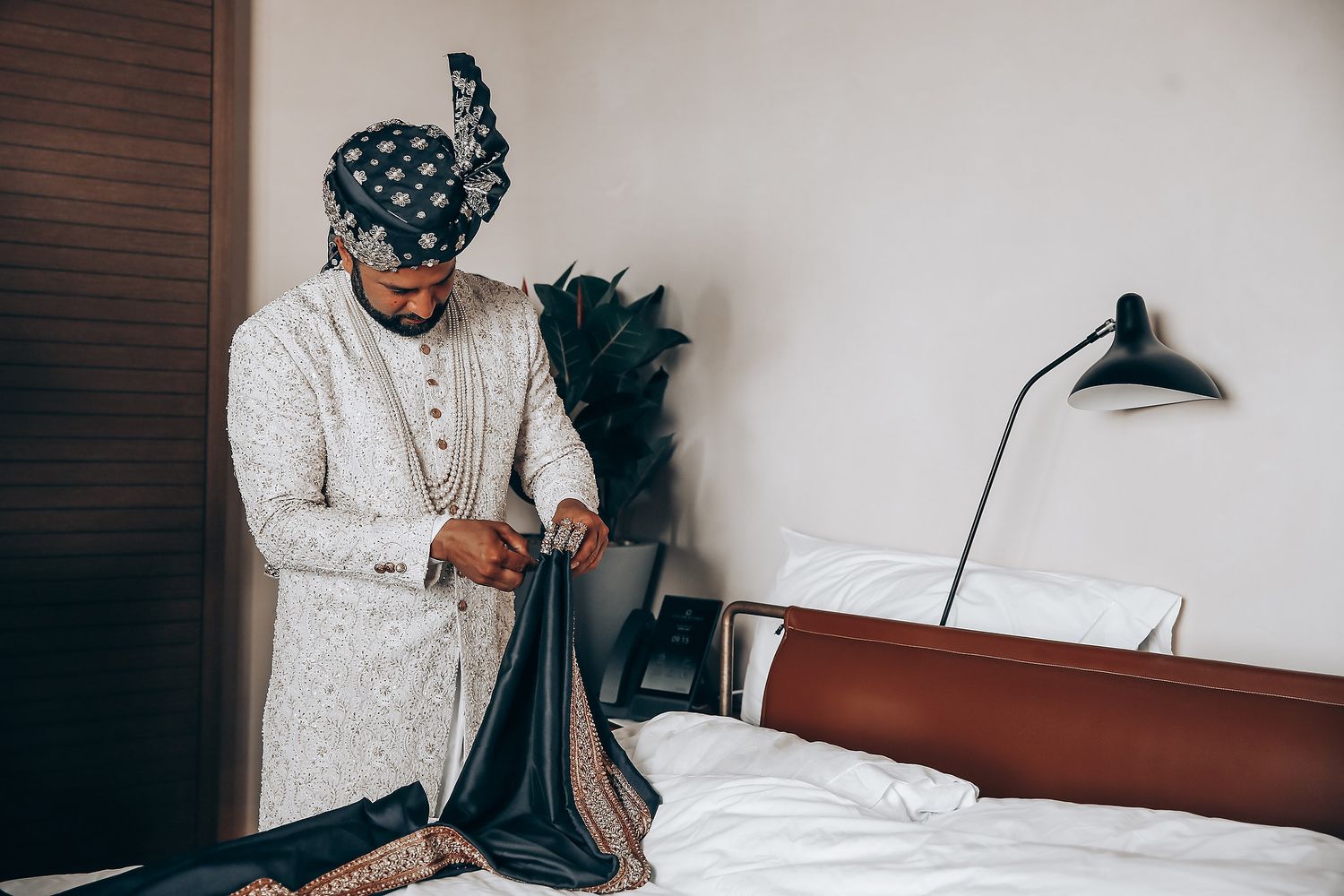 A person in a white embroidered sherwani prepares for a traditional Indian wedding ceremony.