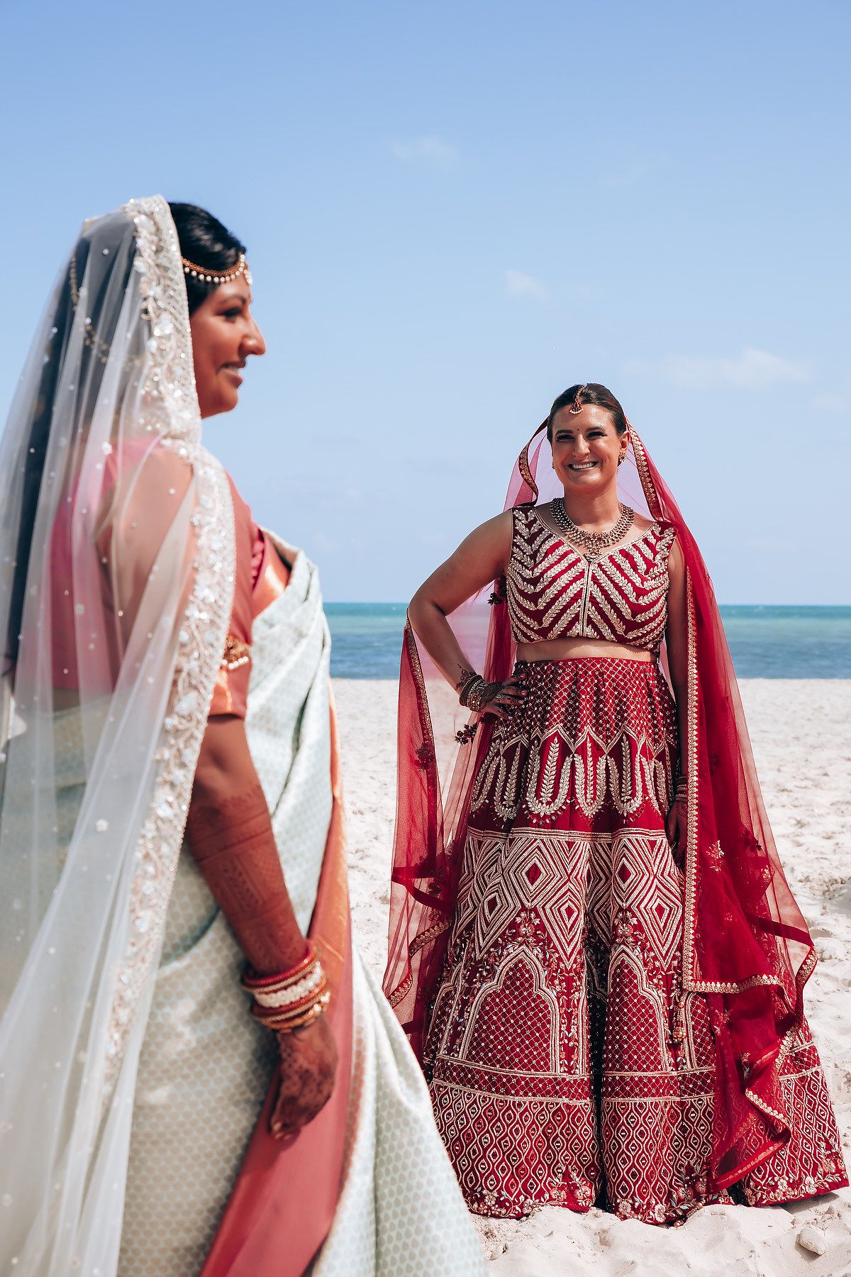 Traditional Indian wedding attire featuring red and white embroidered dresses on a scenic beach.