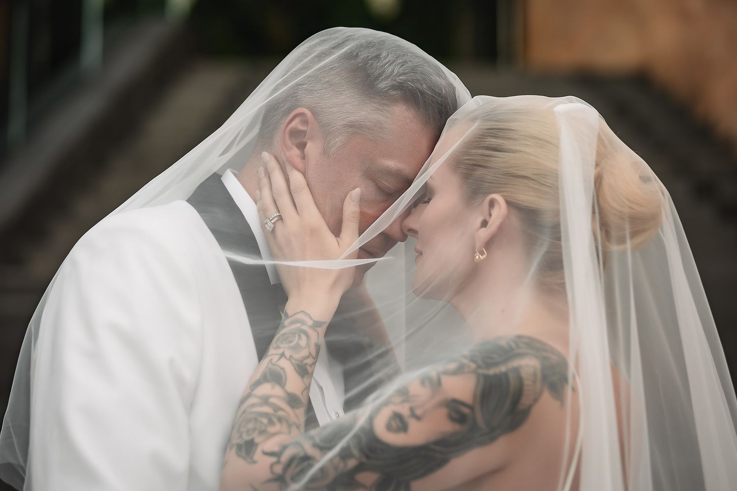 Intimate moment shared under a delicate bridal veil with visible tattoo artwork.