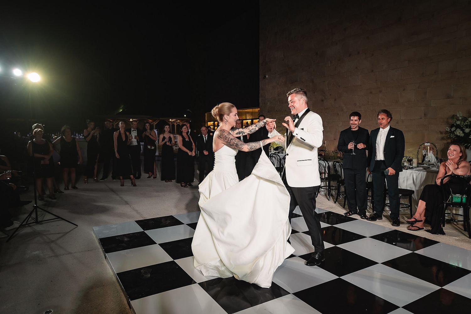 First dance on black and white checkered floor at evening wedding reception.