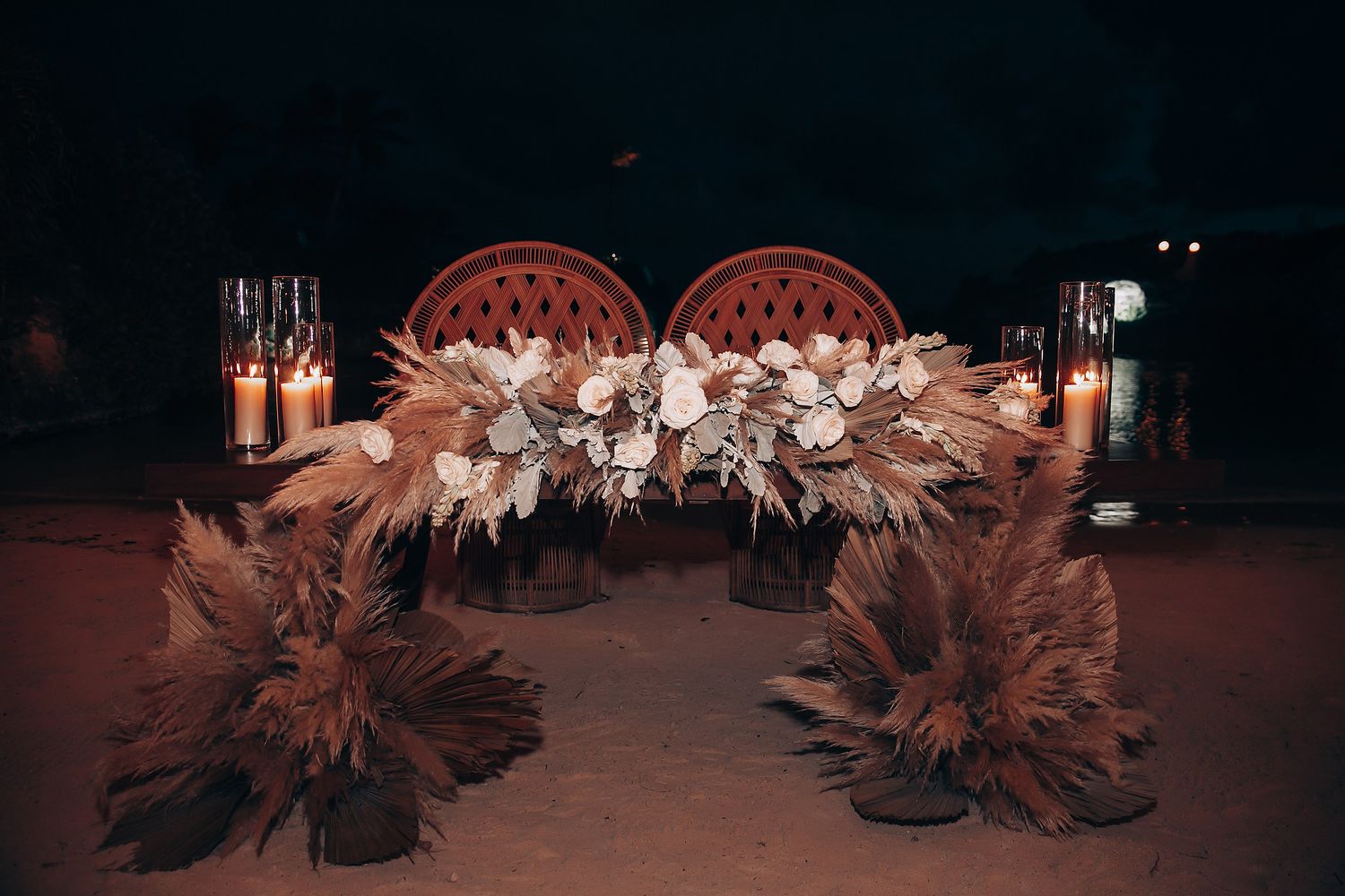 Romantic wedding arch decorated with dried pampas grass and floral arrangements at night.