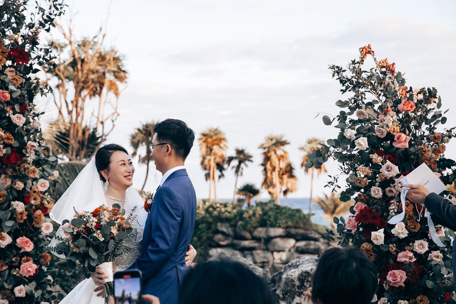 Wedding ceremony moment captured among blooming flowers and palm trees.