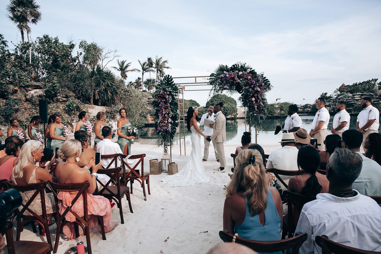 Guests seated at a beachside wedding ceremony with palm trees and ocean views.