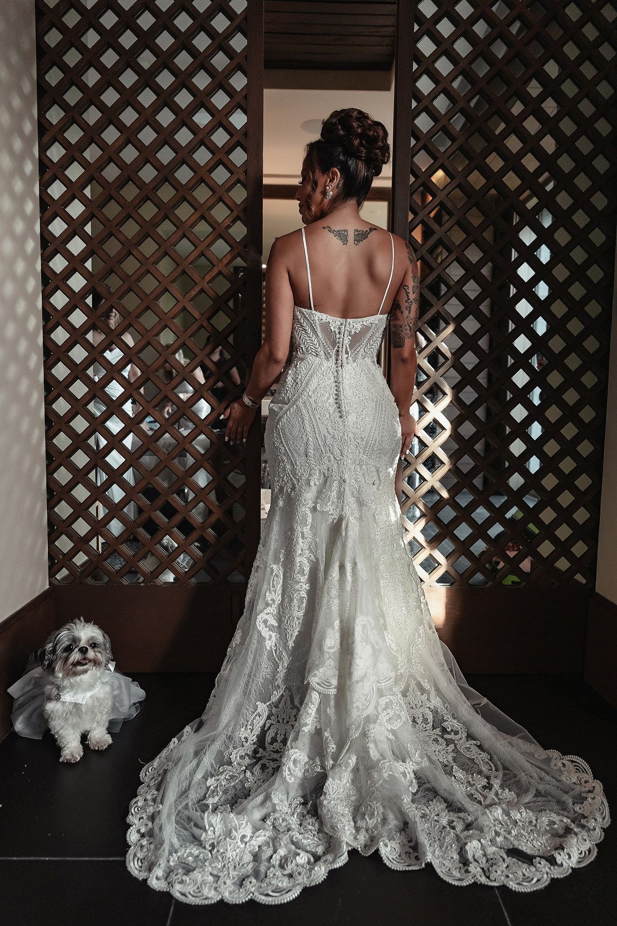 Intricate lace wedding dress train displayed against dark lattice background.