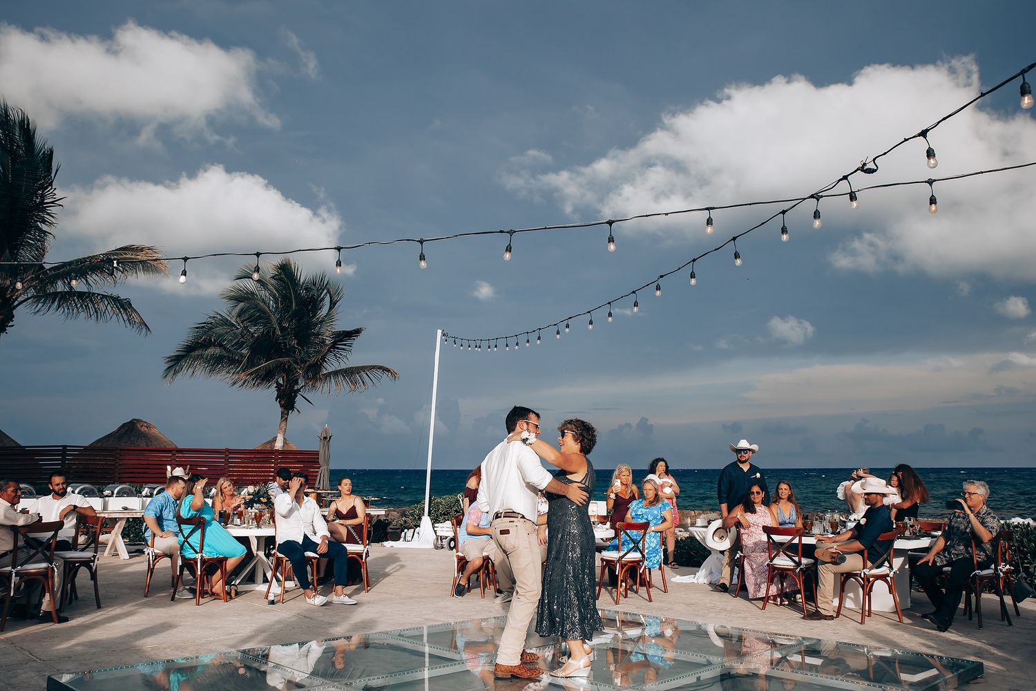 Festive outdoor celebration with string lights and palm trees against a bright blue sky.