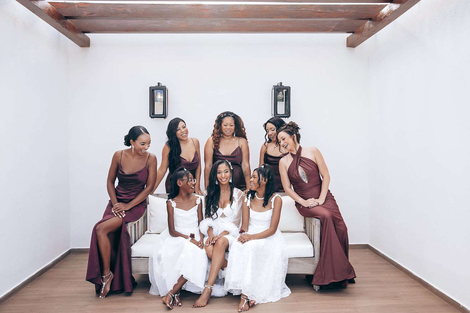 Wedding party members in burgundy dresses and white gowns gather in a bright indoor space.
