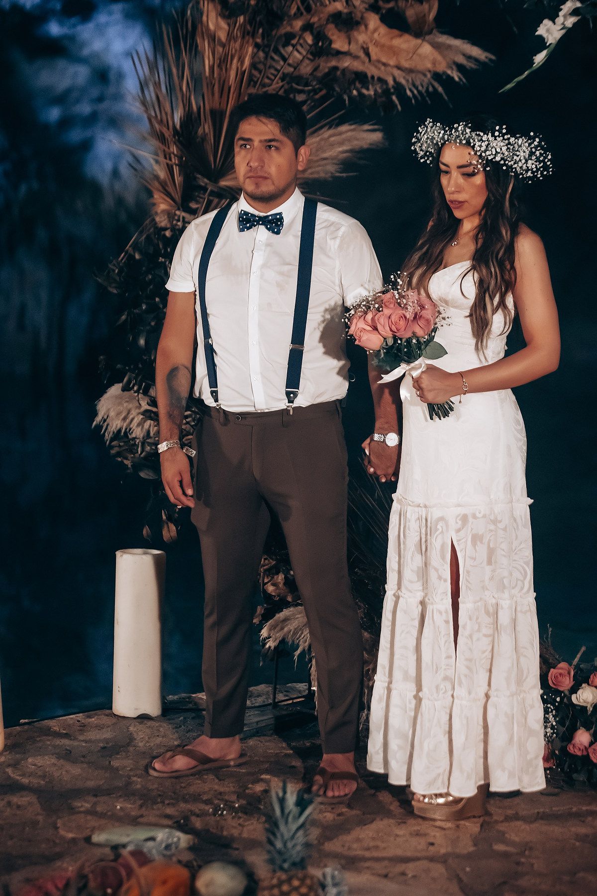 A romantic wedding photo in a cave setting with dried pampas grass decor and a couple in boho-style attire.