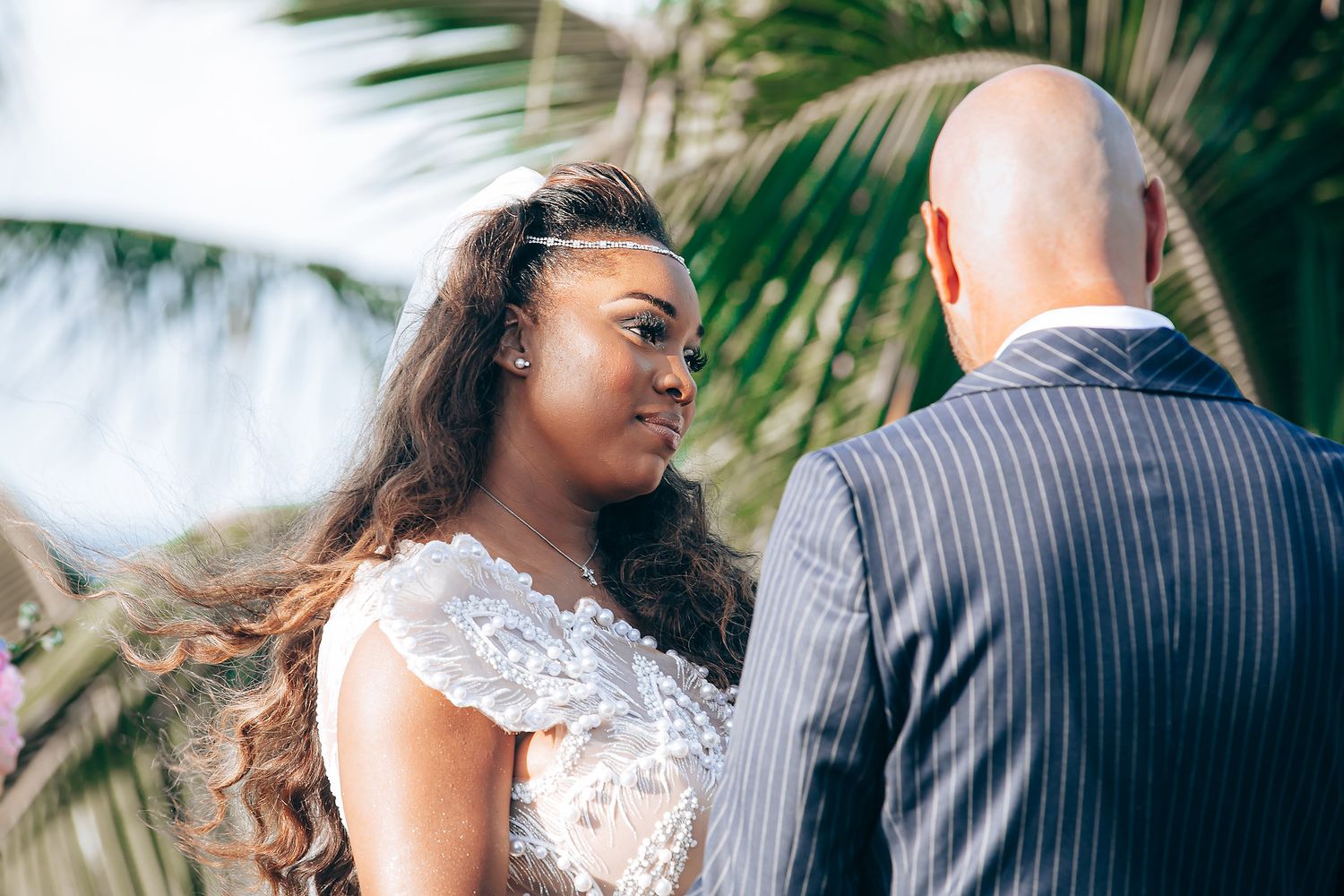 A couple shares a tender moment at their outdoor wedding ceremony with palm trees in the background.