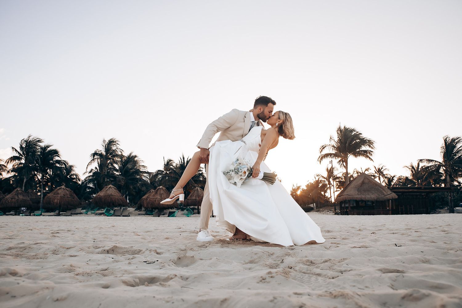 Newlyweds sharing intimate moments on a tropical beach at sunset.