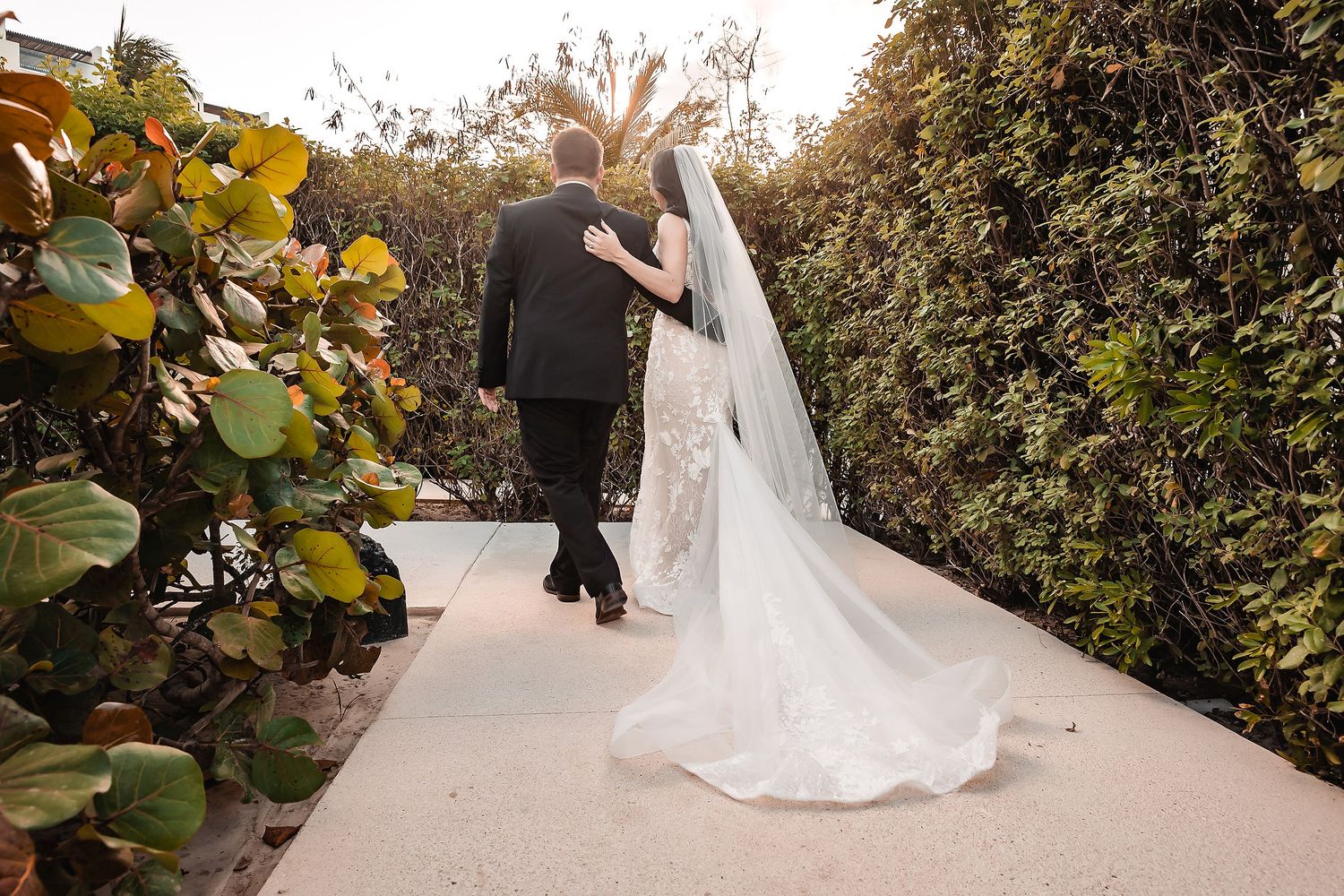 A wedding couple poses in a lush garden setting with greenery and flowers.