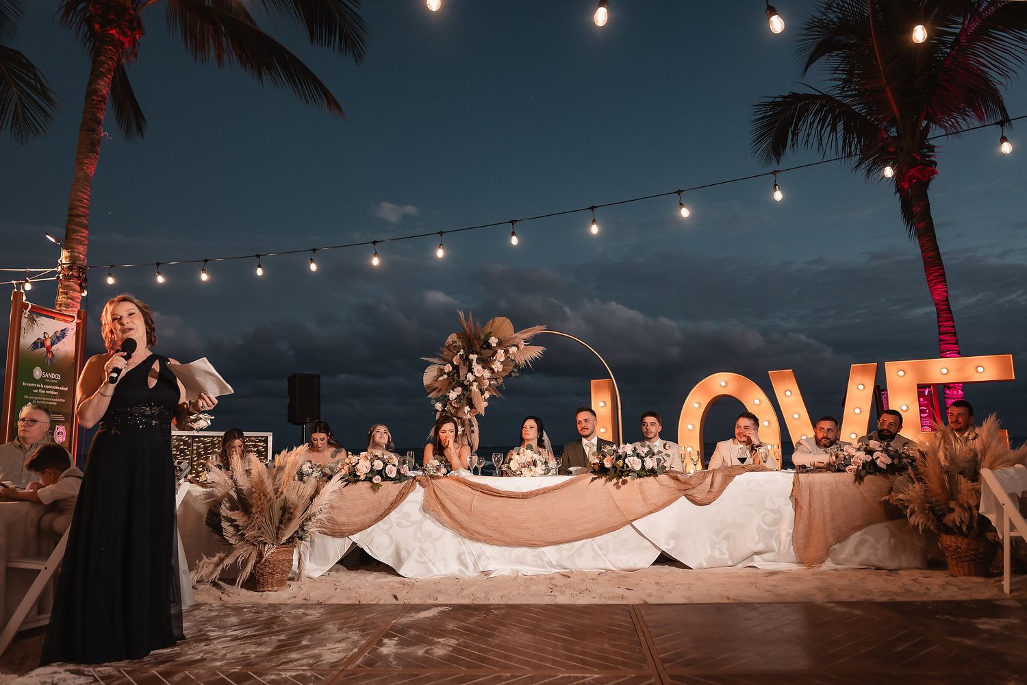 Nighttime beach wedding celebration with illuminated LOVE sign and string lights.
