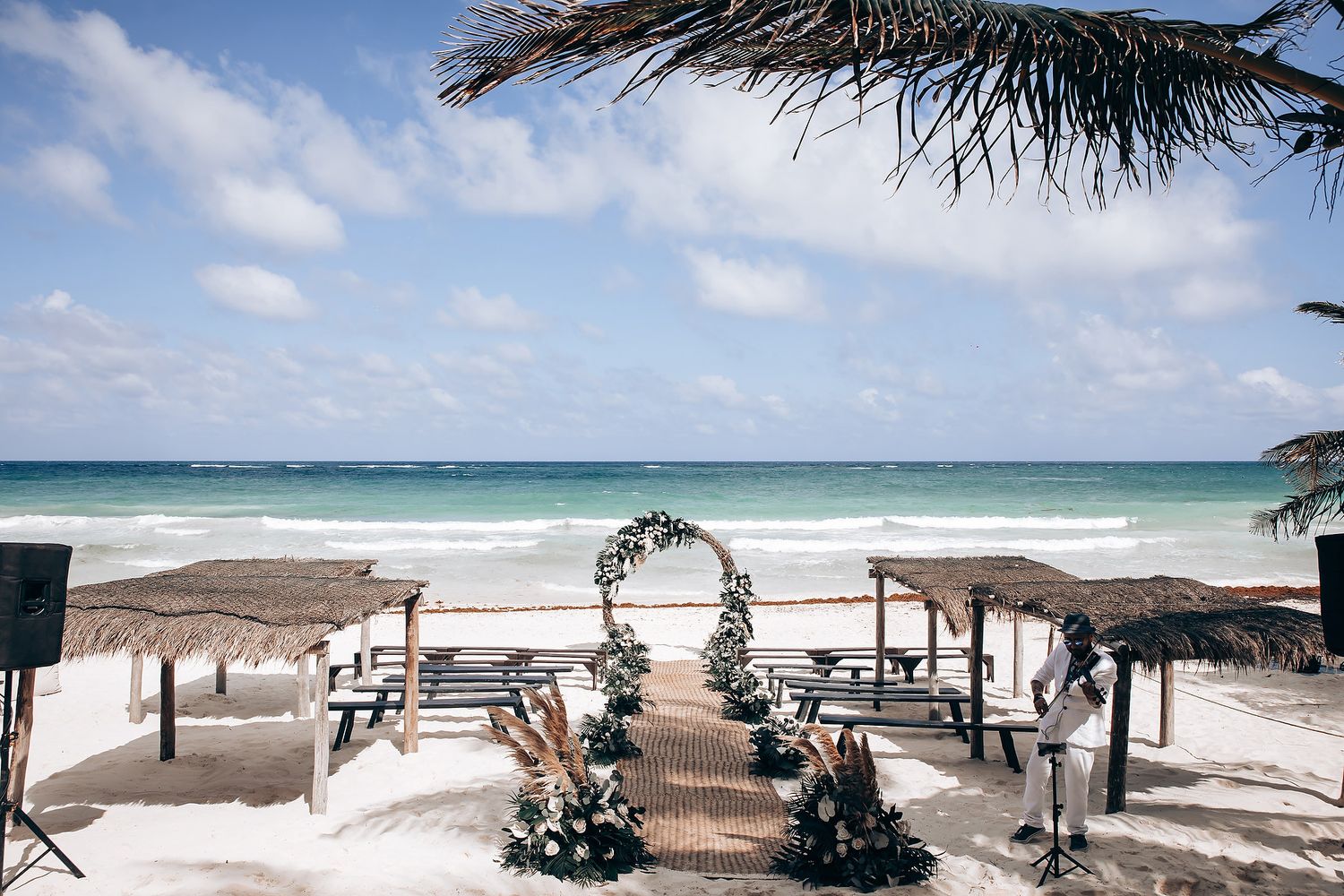 A panoramic view of a beach wedding setup with wooden benches and floral arch decorations.
