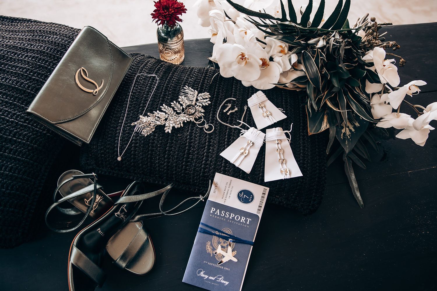 Wedding accessories including passports, flowers, and jewelry arranged on dark surface.