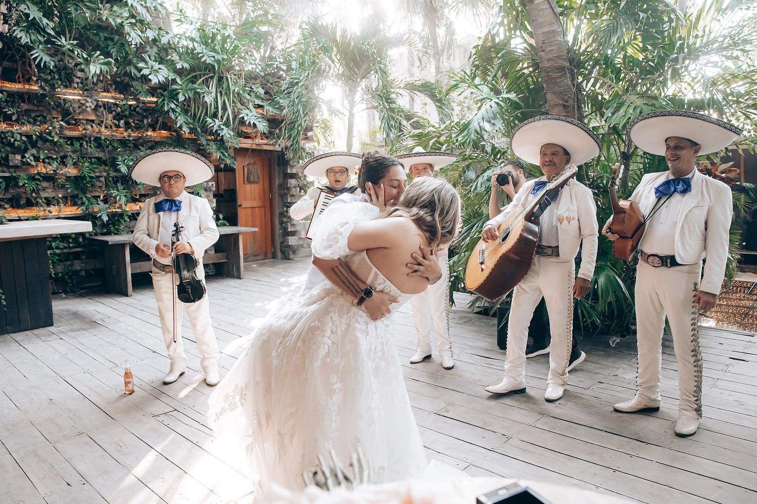 Wedding celebration with guests in light colored attire dancing on a wooden deck.