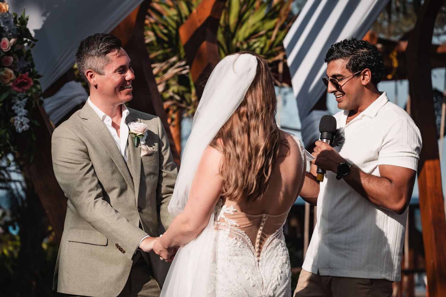 Wedding ceremony moments captured under wooden arch with coastal scenery in background.