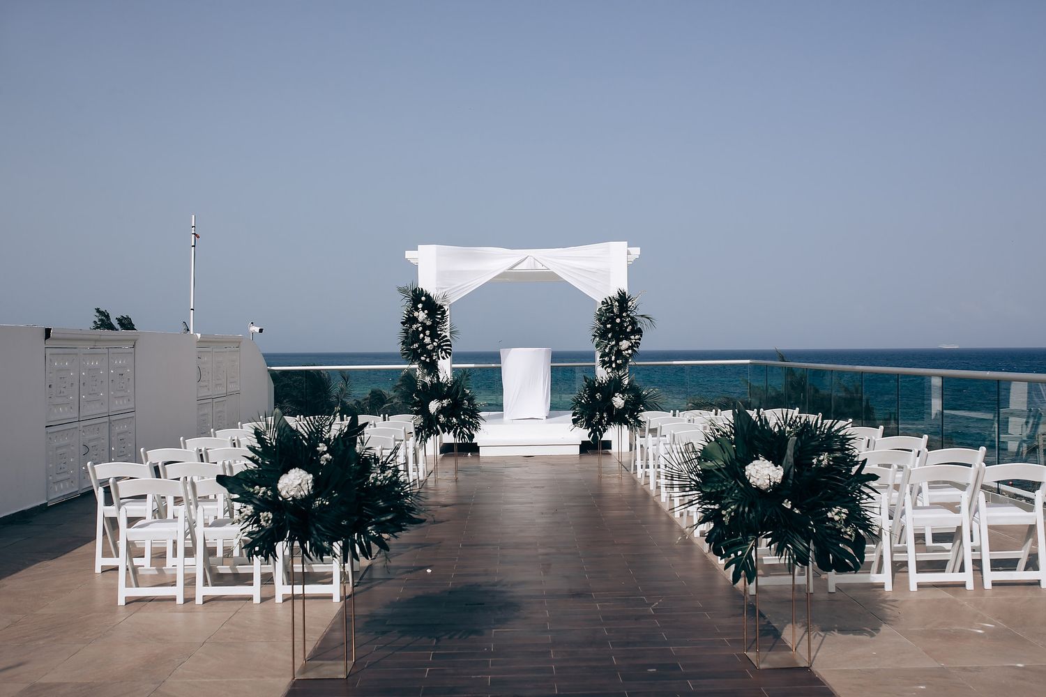 Minimalist white wedding ceremony space with wooden deck and tropical ocean views.