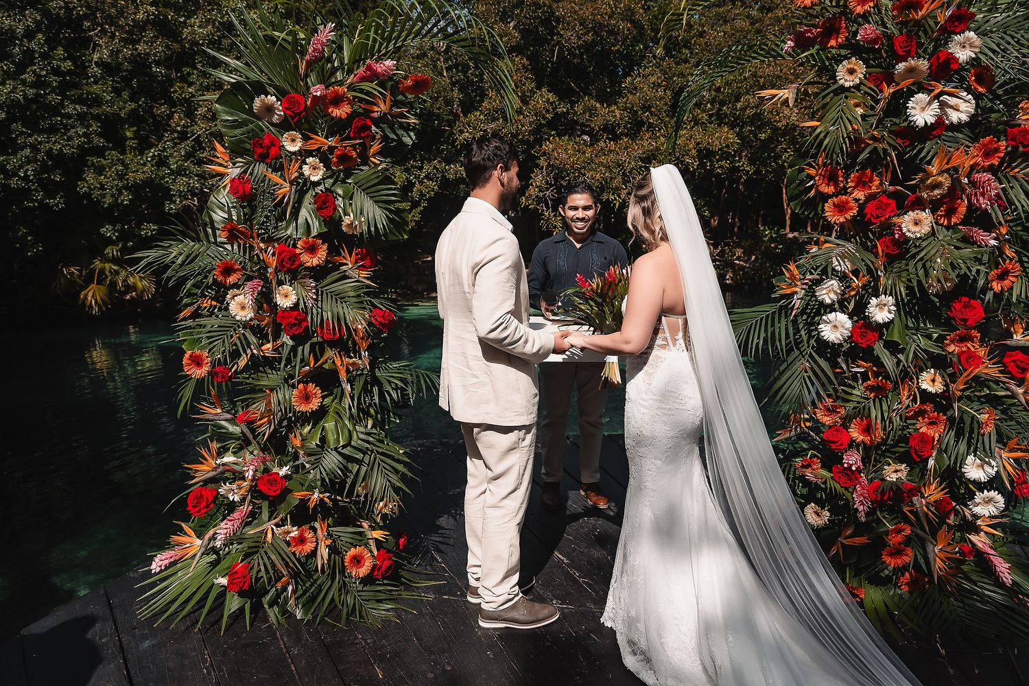 Elegant wedding ceremony setup with dramatic red and white floral arrangements in tropical garden.