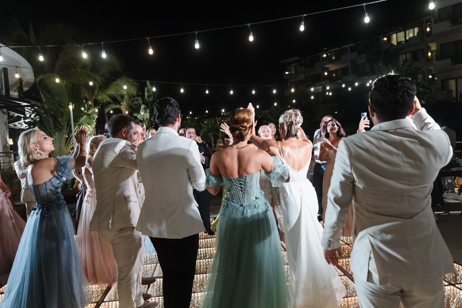 Elegant wedding reception outdoors at night with guests dancing under string lights in formal attire.