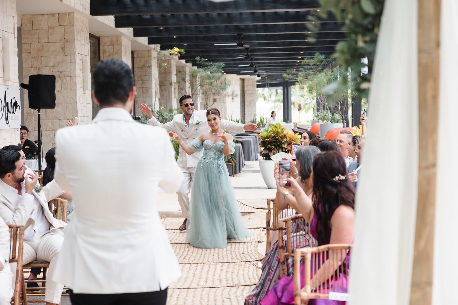 Bride and groom walk down outdoor wedding aisle at elegant venue as guests celebrate and photograph the moment.