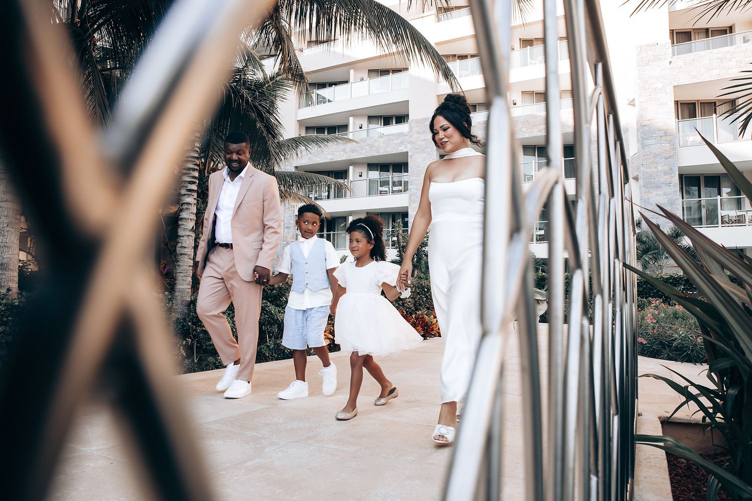 A family walks together outdoors in coordinated light-colored outfits near a modern building.