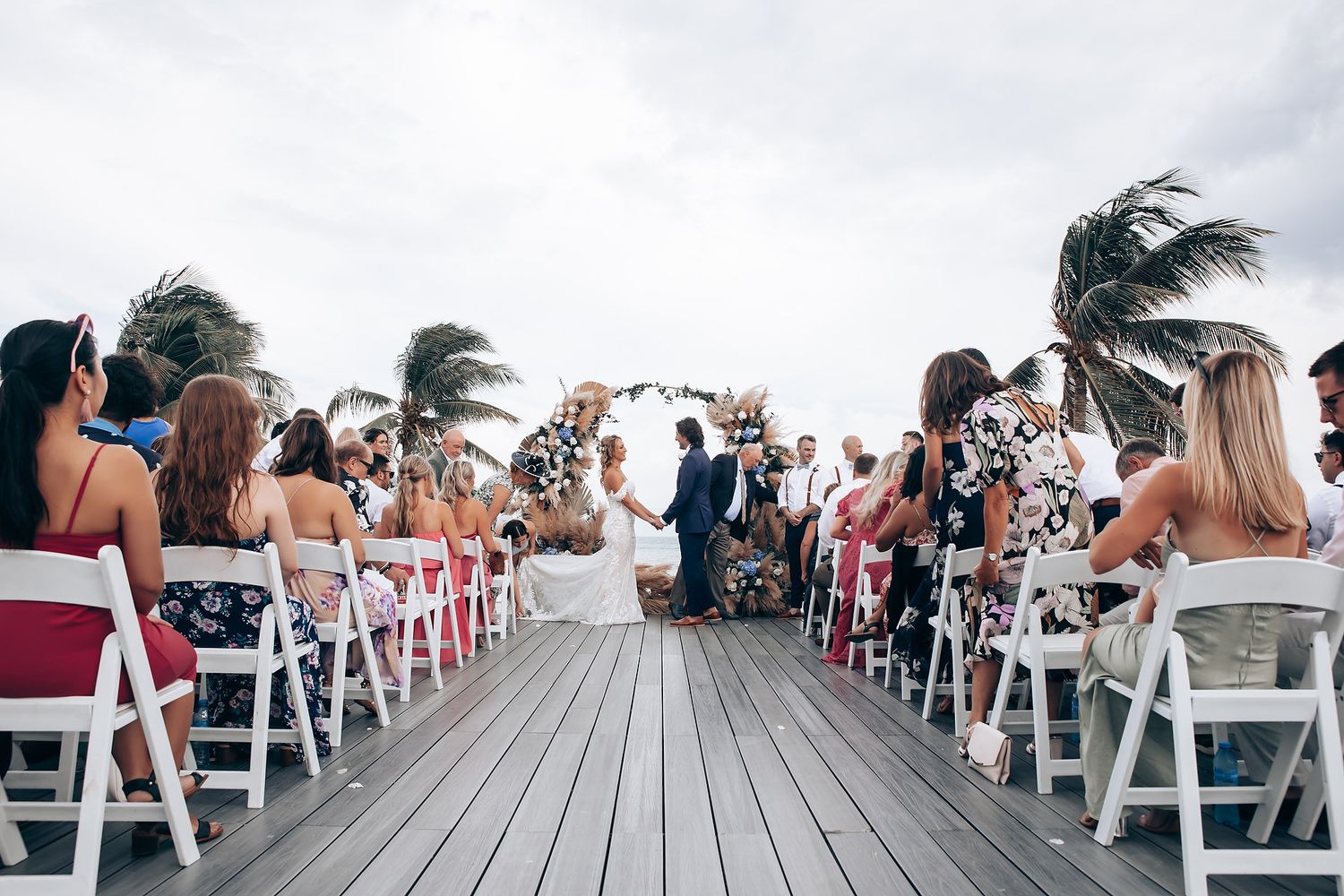 White folding chairs line a wooden deck for an oceanfront wedding ceremony.