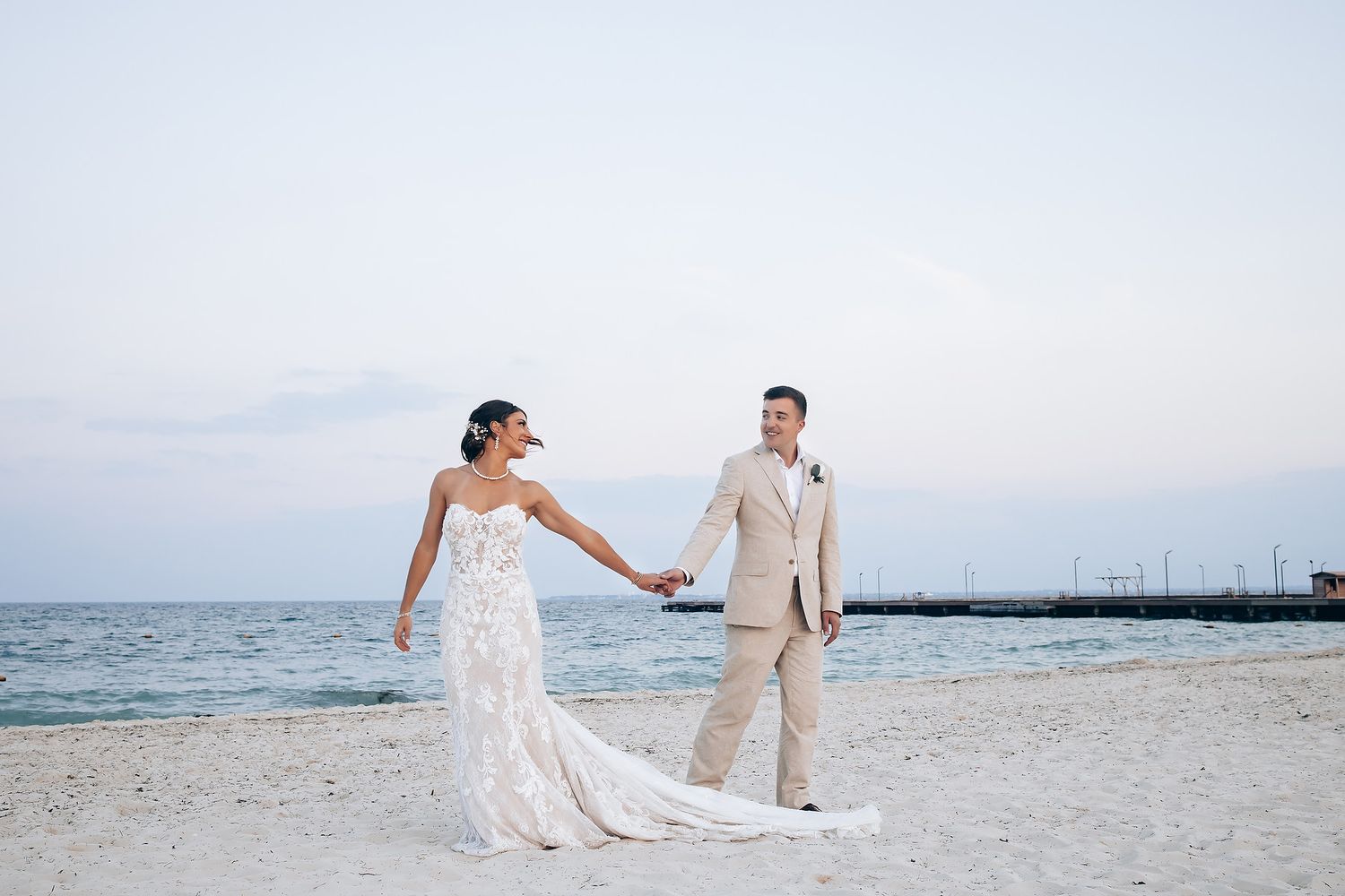 Playful wedding photography session on a white sandy beach with ocean waves in the background.