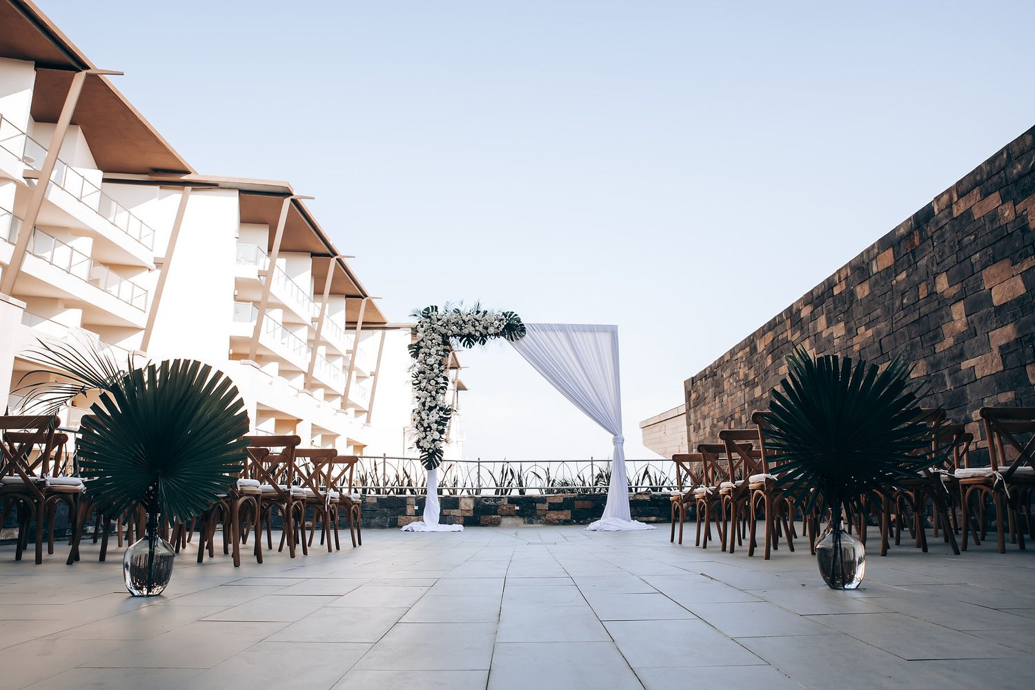 An elegant wedding ceremony setup with white draping and floral arch against an ocean view.