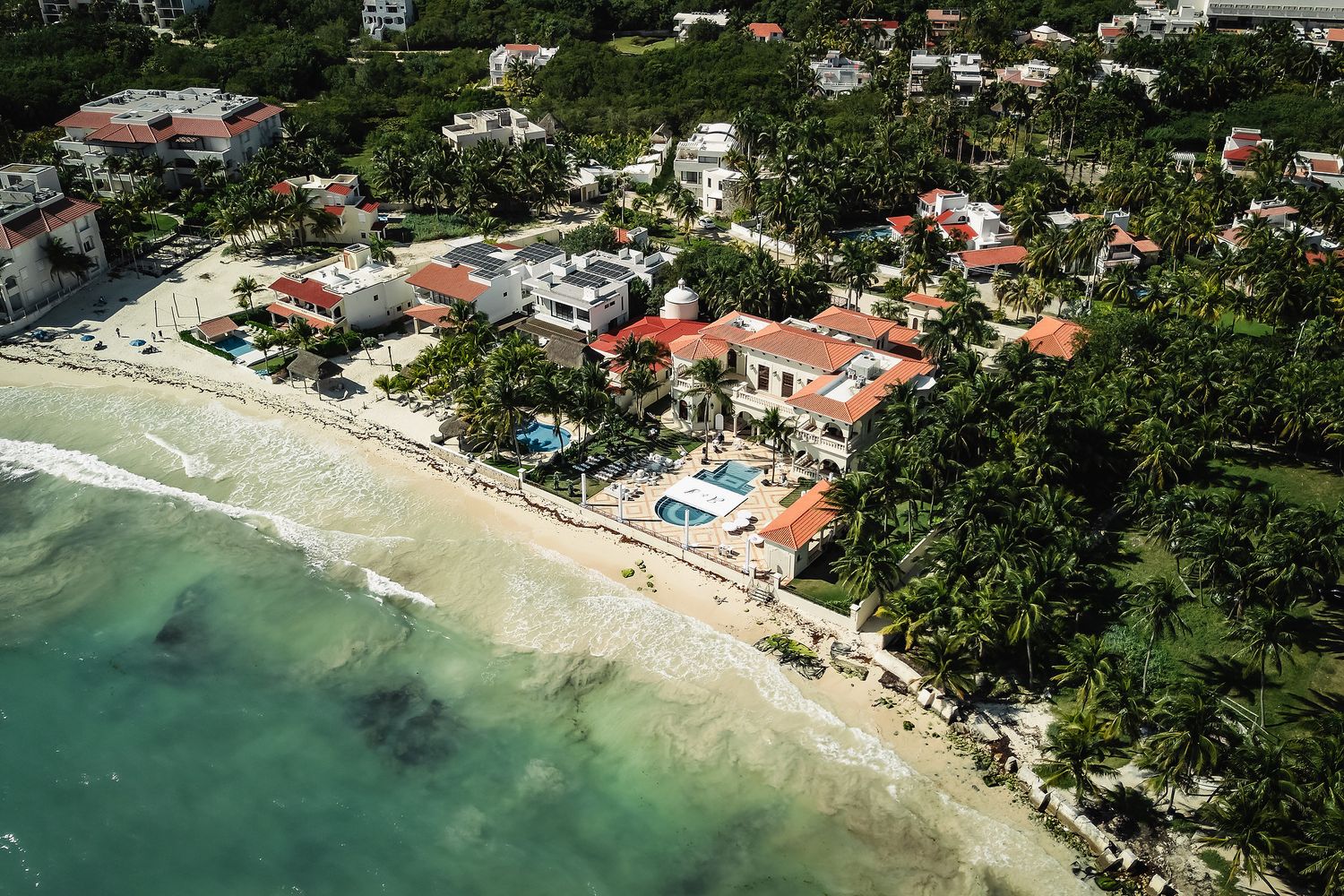 Aerial view of coastal town with white buildings and turquoise waters along beach.