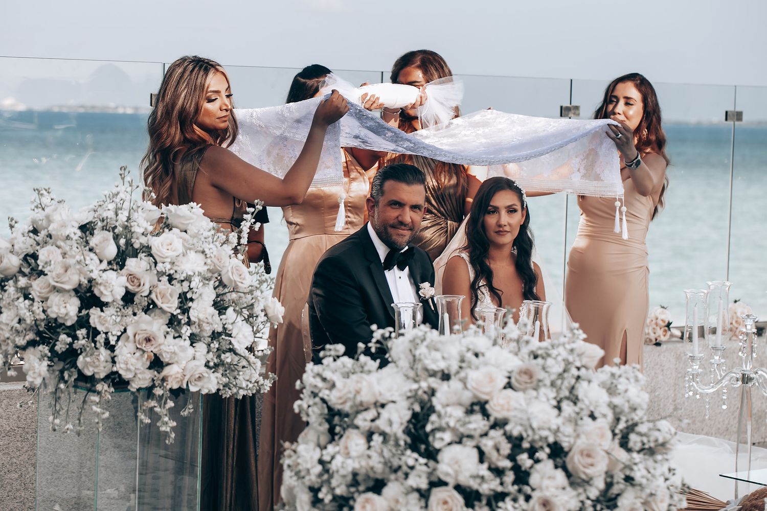 Elegant wedding reception setup with white floral arrangements and ocean view backdrop.
