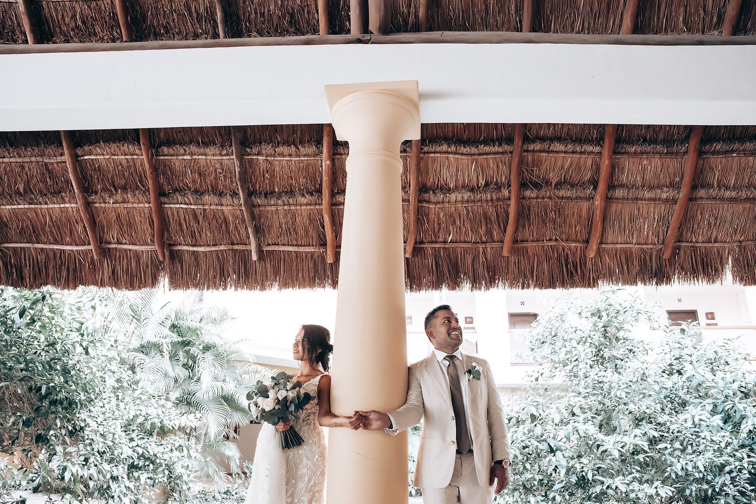 Outdoor wedding ceremony setup with wooden chairs and palm trees under a thatched roof palapa.