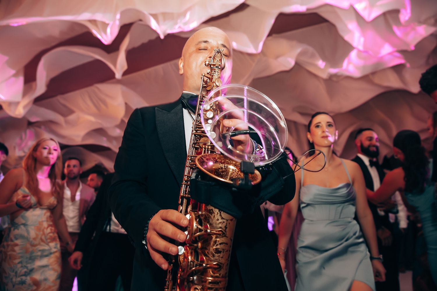 Wedding reception dance party with live saxophone music and pink lighting creating a festive atmosphere.