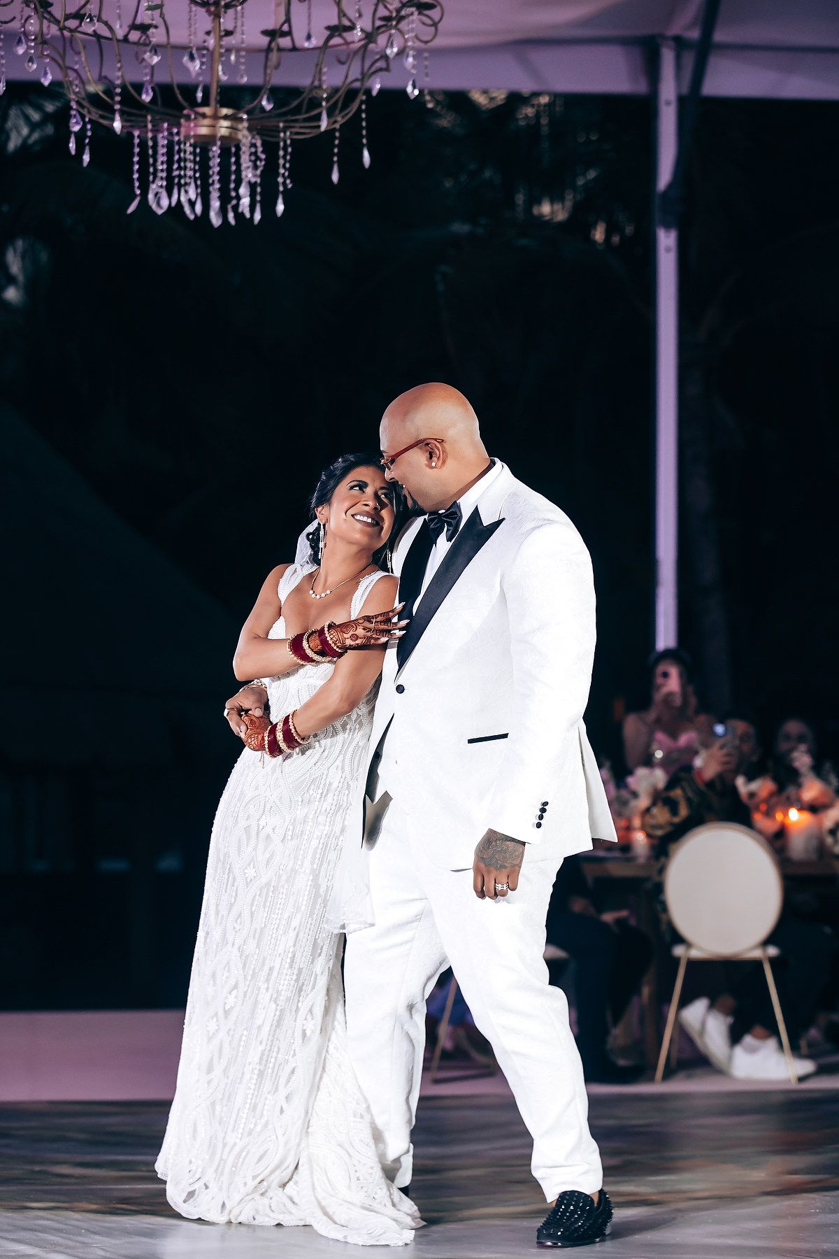 A couple shares an intimate dance moment at their wedding reception under elegant chandeliers.