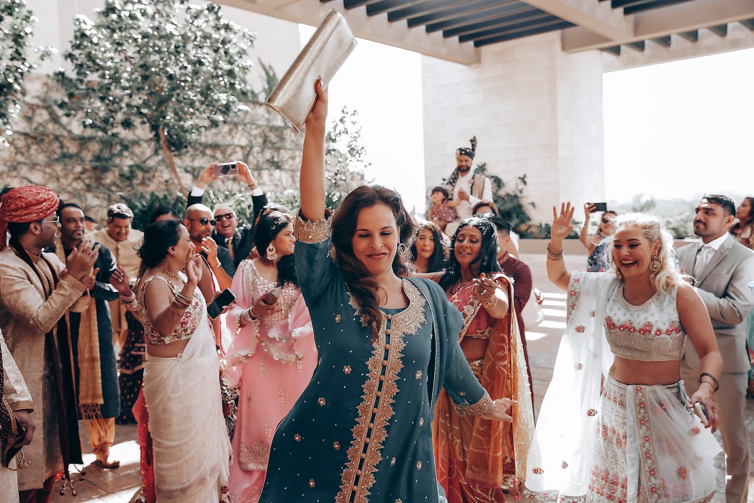 Wedding guests celebrate and dance together during a joyful outdoor reception under a wooden pergola.