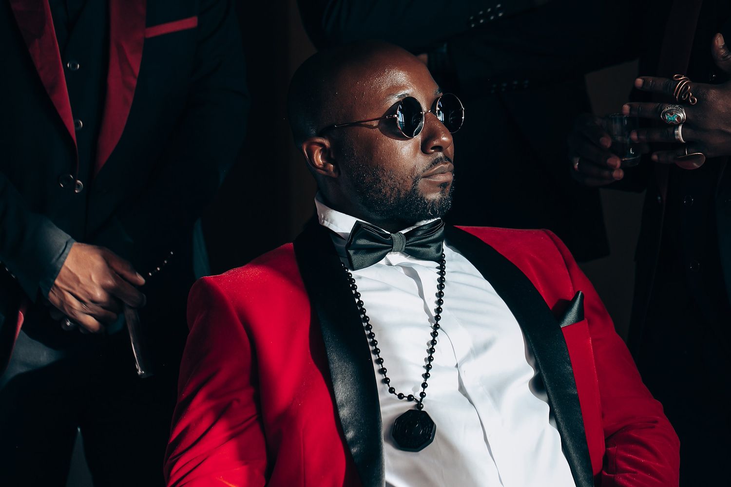 People wearing red jackets and sunglasses pose in stylish formation against dark background.