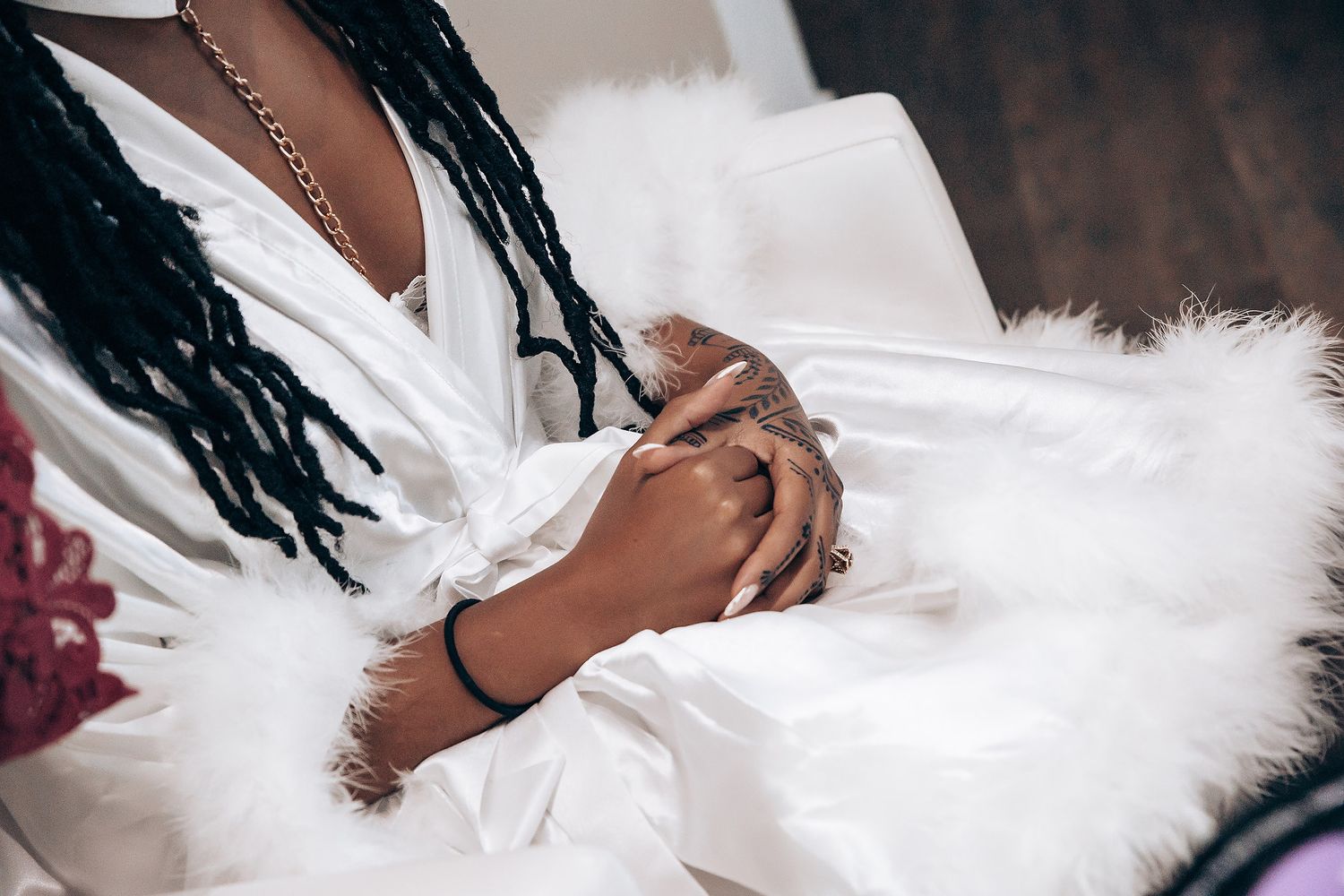 A person wearing black braids gently holds a white feather boa against a dark background.