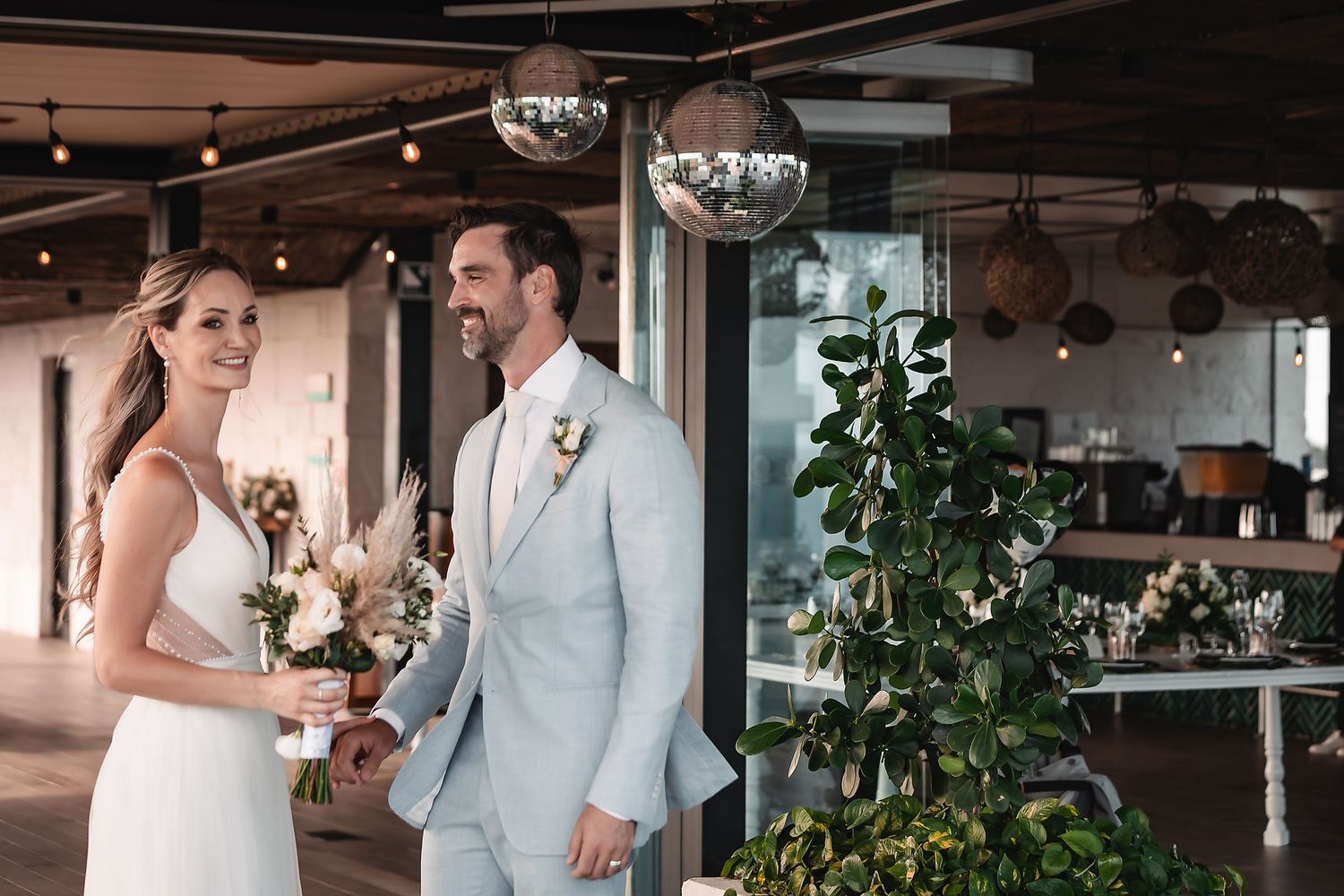 Modern indoor wedding reception venue decorated with hanging lights and greenery.