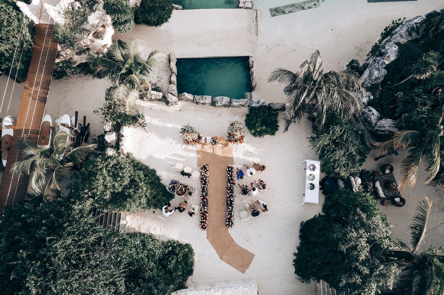 Aerial view of a tropical beach wedding ceremony setup with white chairs and floral arrangements.