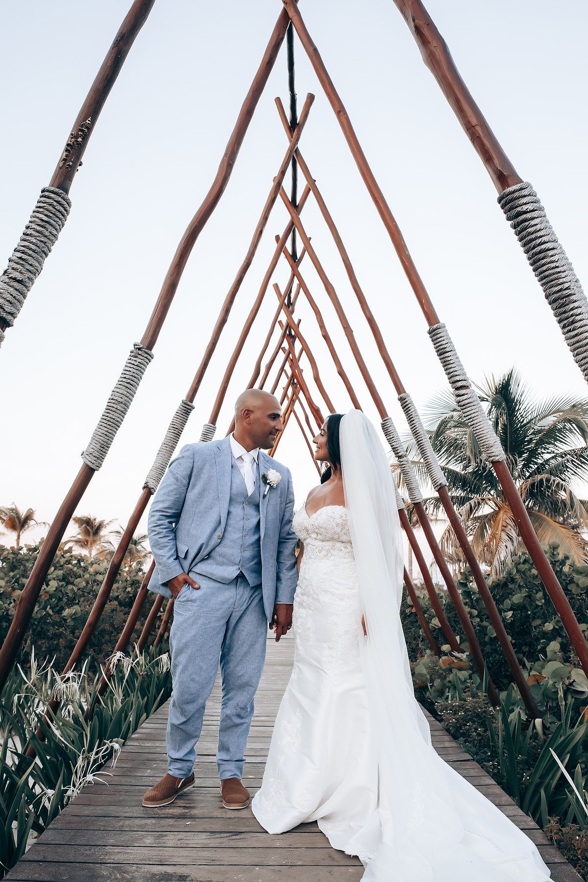 Wedding couple walking on wooden bridge with tropical palm decor.