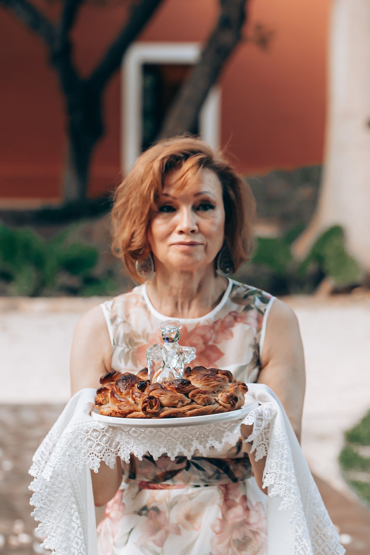 Woman in white lace dress holding plate of chocolate cake in outdoor setting with blurred background.