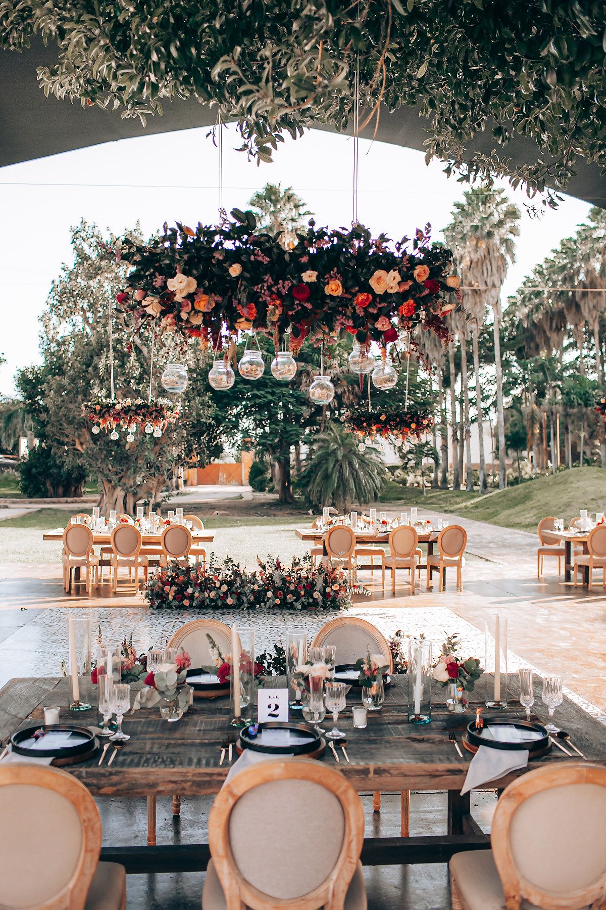 Elegant table settings with vintage chairs and floral arrangements under a canopy for an outdoor wedding reception.