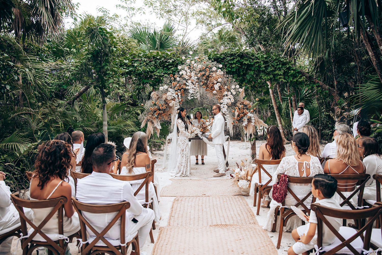 A panoramic view of a wedding ceremony in a lush garden setting with guests seated in wooden chairs.