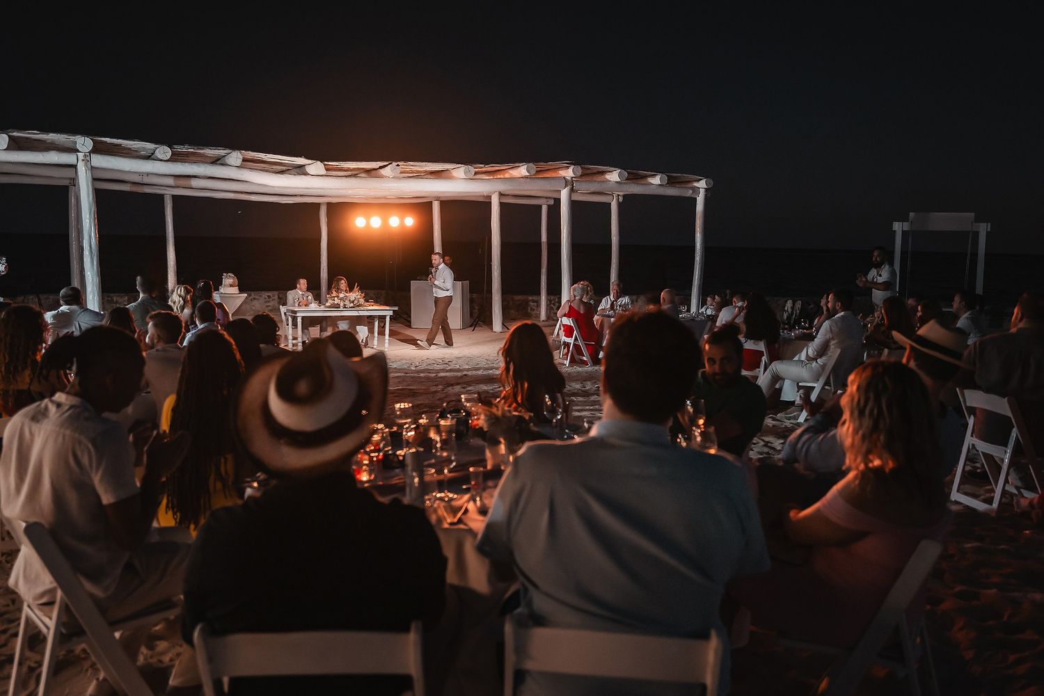 Evening wedding reception under string lights with a dark, moody atmosphere.
