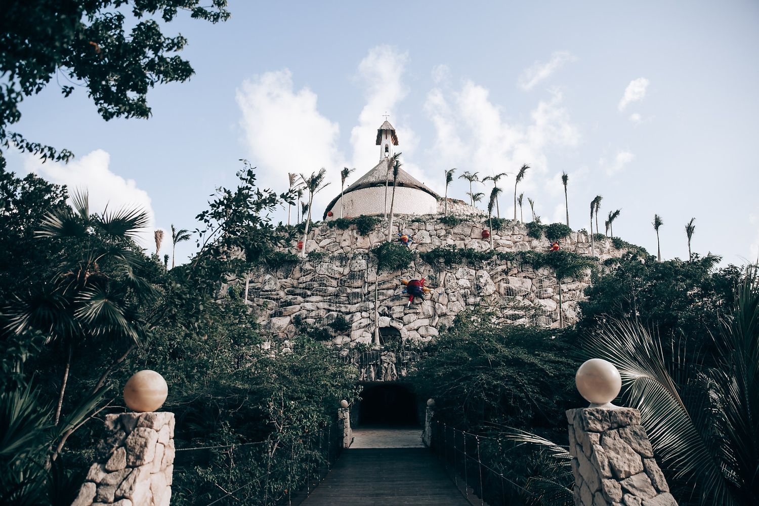 Stone pathway leads to domed building with ornate architecture and tropical landscaping.