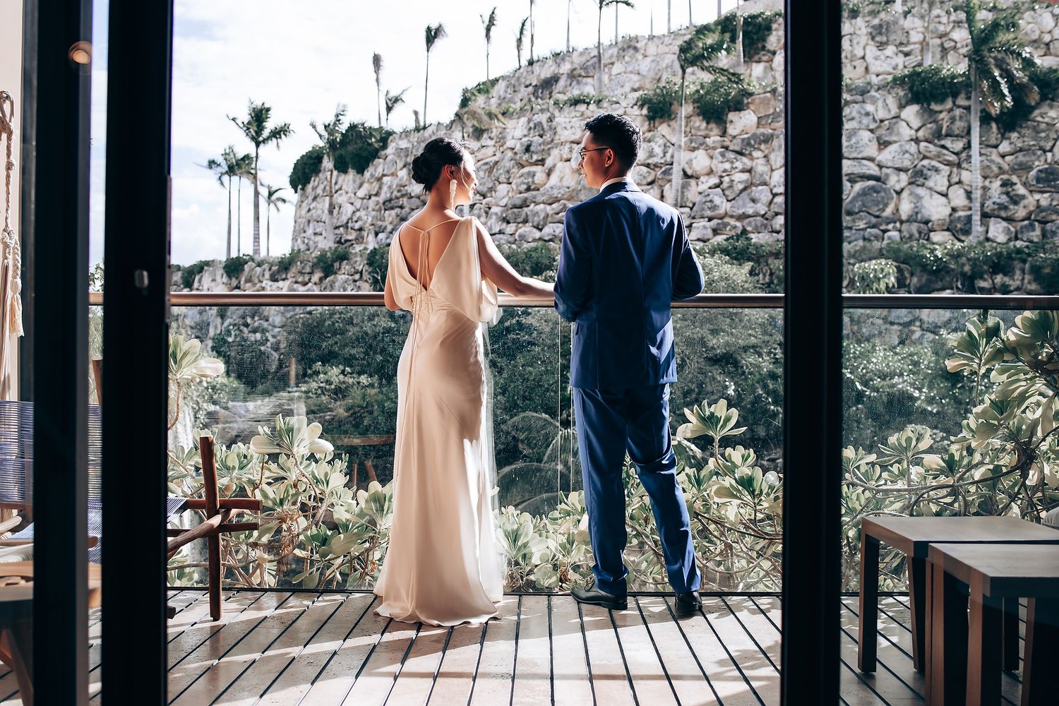 A couple stands on a wooden deck overlooking a scenic mountain landscape during a wedding celebration.