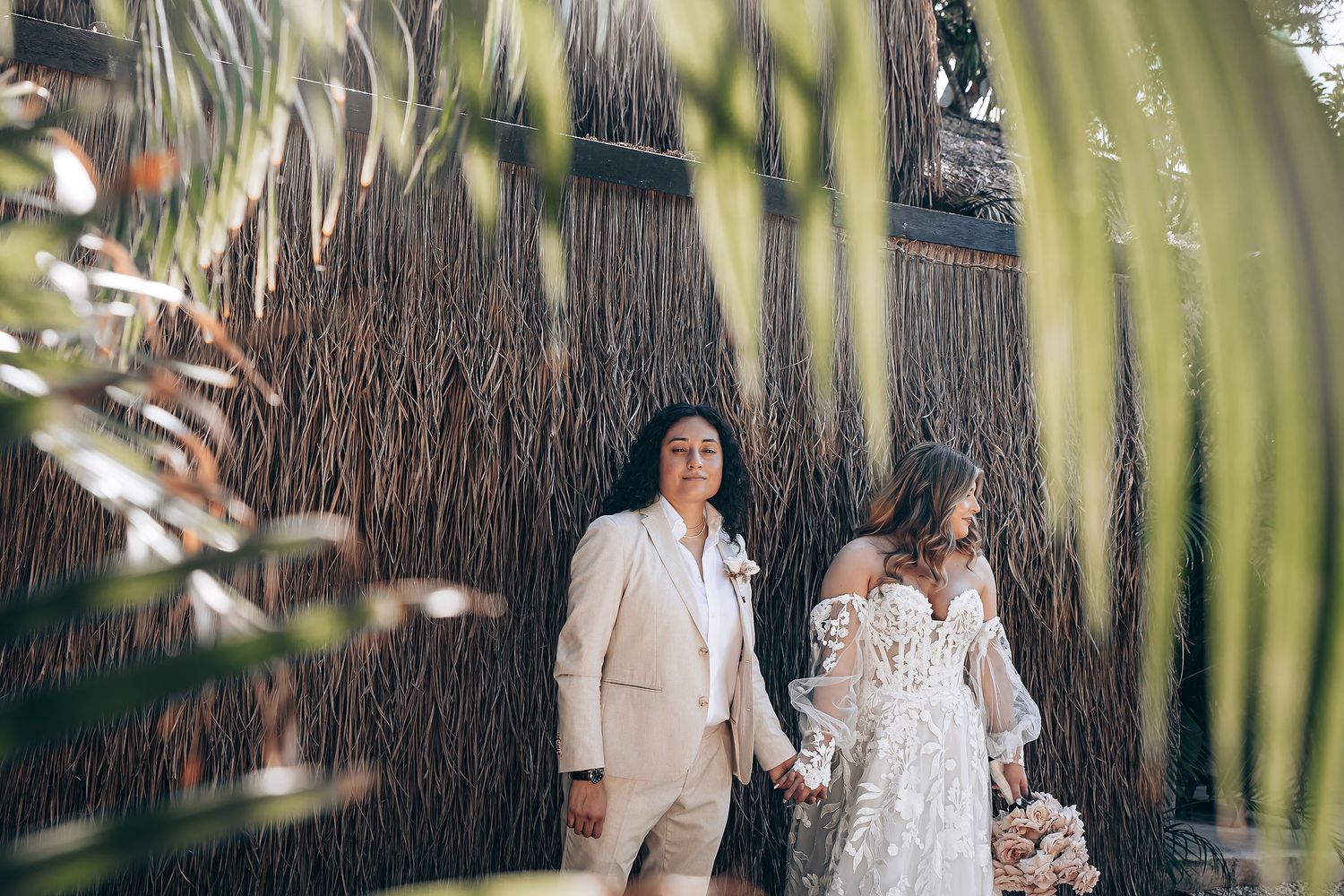 Couple walking through a lush garden setting with palm fronds creating a natural frame around them.