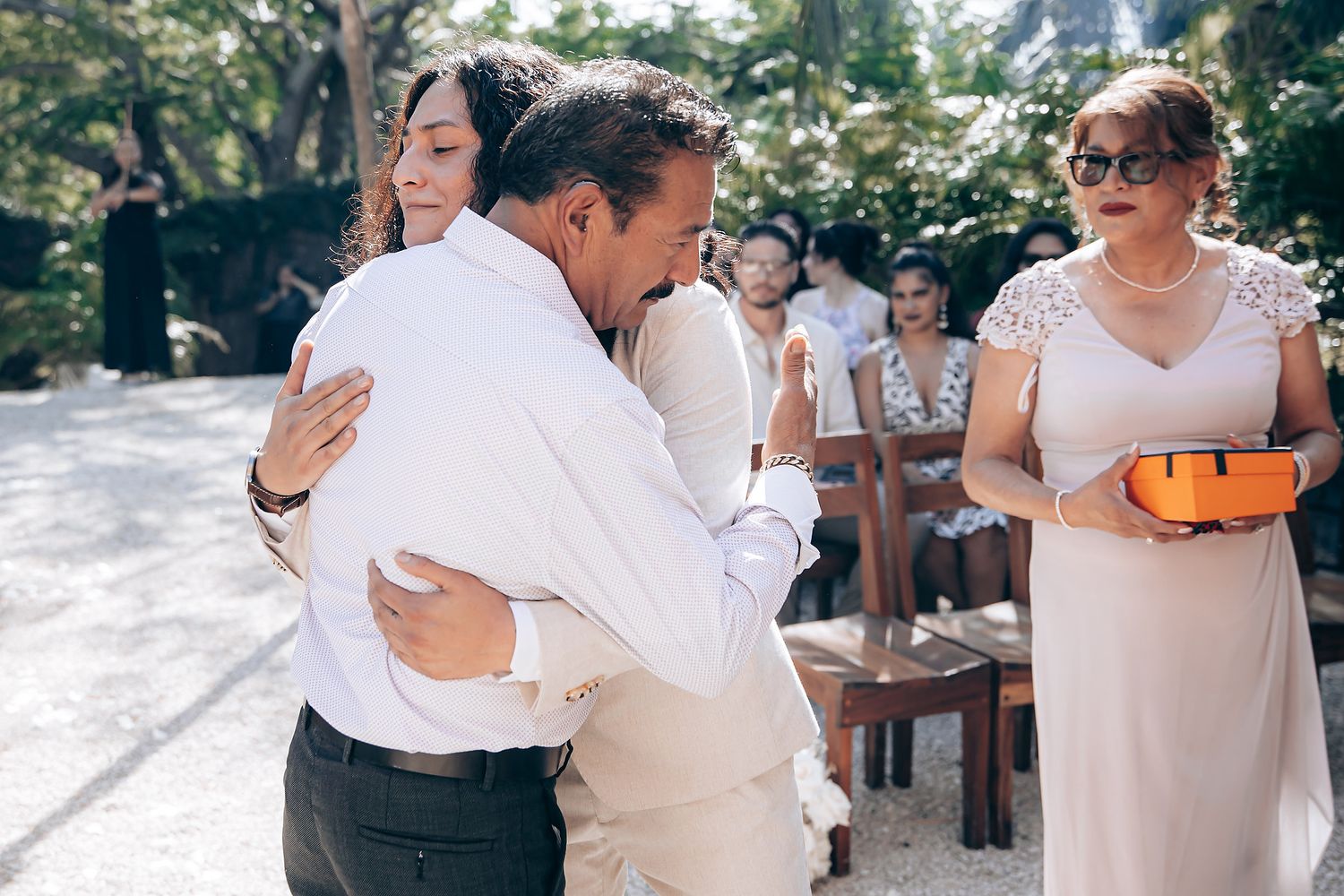 A couple shares a romantic dance moment at an outdoor wedding celebration surrounded by guests and natural scenery.