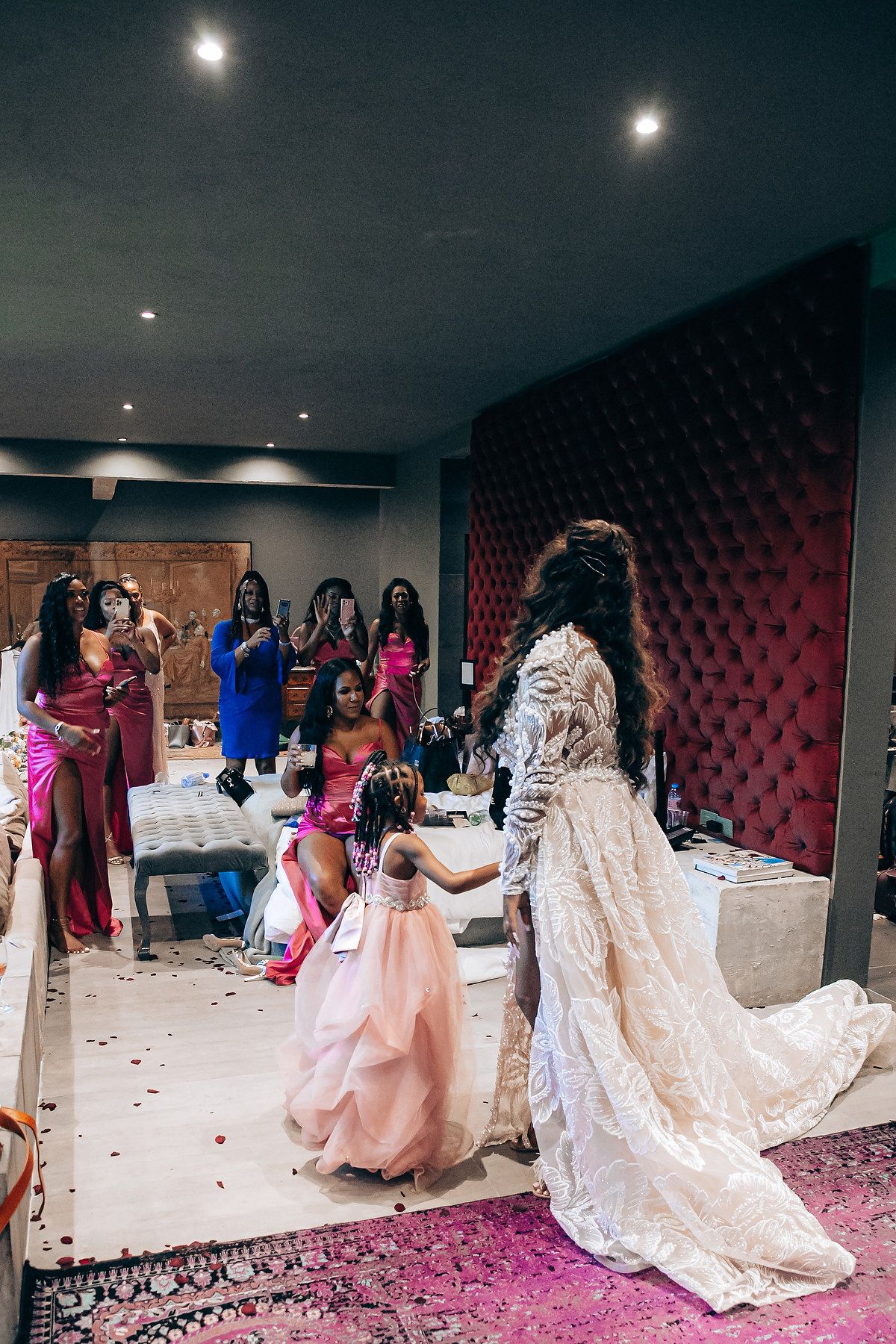 A festive wedding celebration shows people in colorful formal attire gathered around a bride in a flowing lace gown.