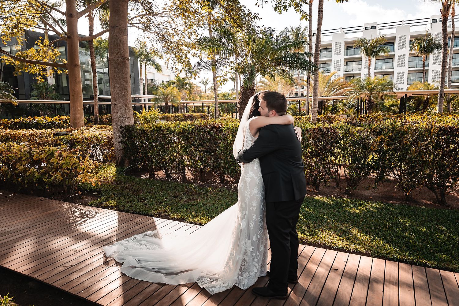 A romantic first look moment between newlyweds on a wooden deck surrounded by palm trees and gardens.
